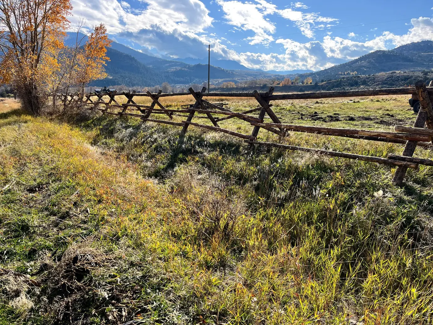 Bark-on jackleg fence line crossing uneven Montana terrain