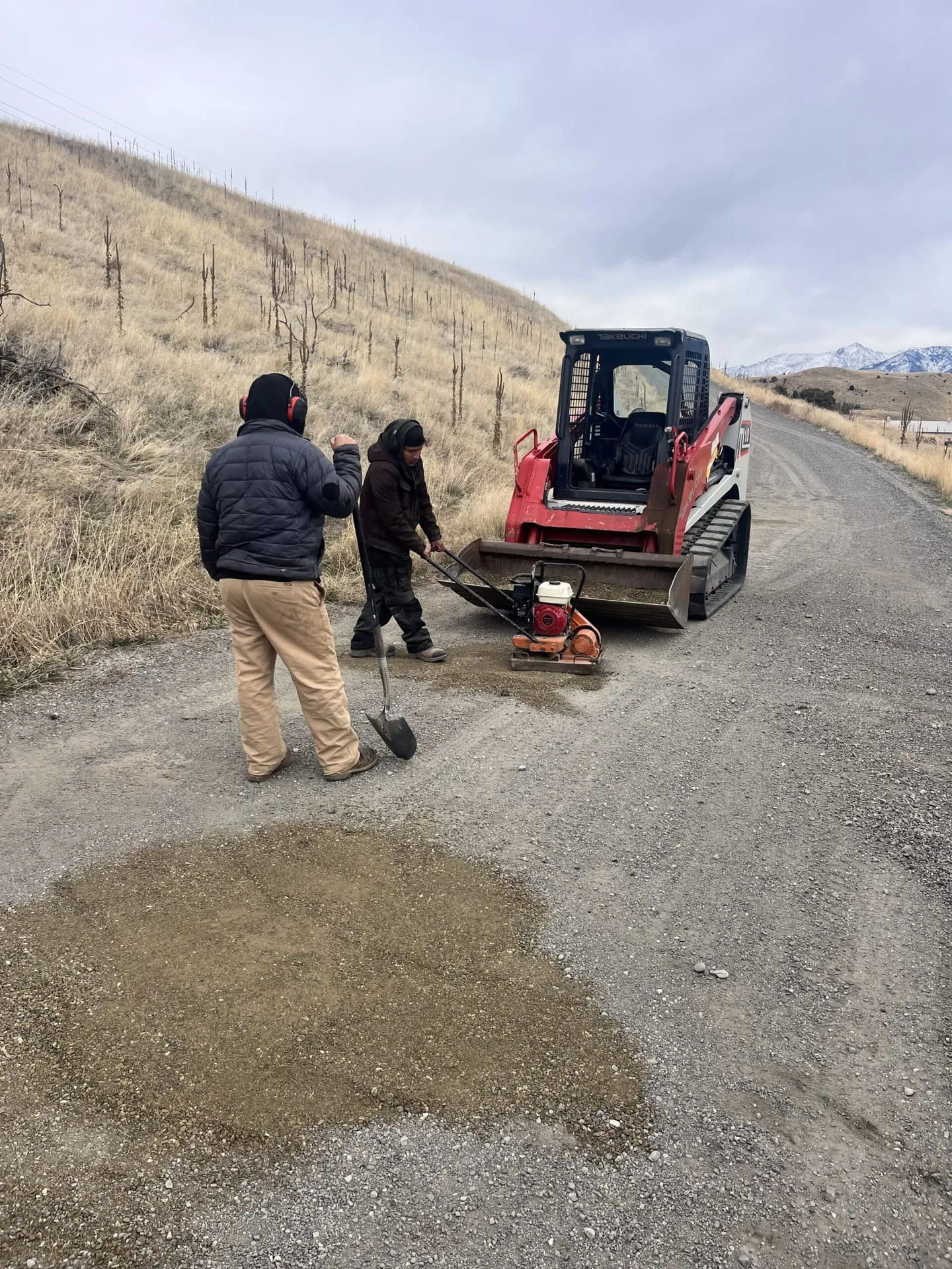 Crew repairing a soft, water-worn spot on a gravel road with a compactor
