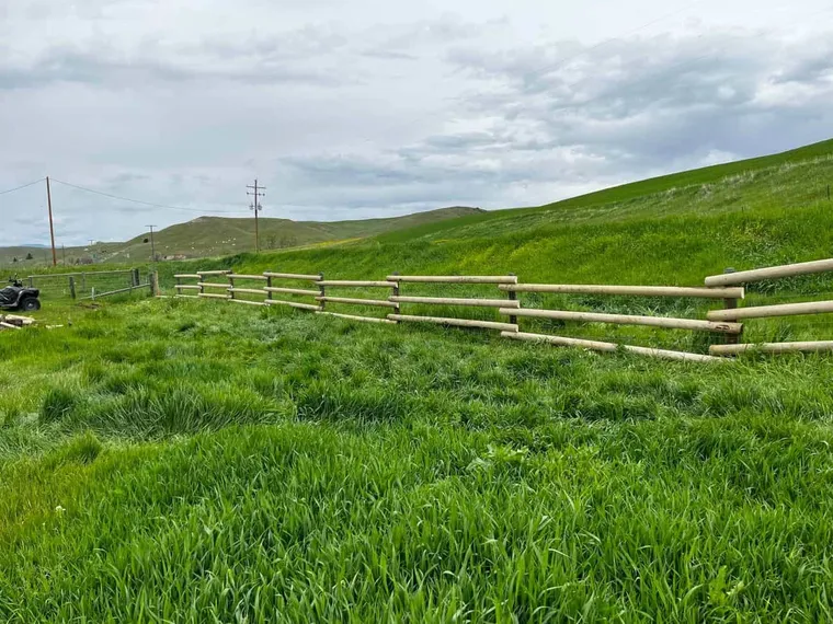 New round-rail fence running up a green Montana hillside, built by Montana Ranch & Land Improvement Service
